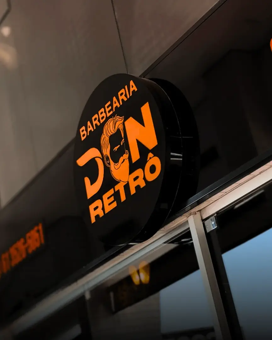 Letreiro redondo da Barbearia Don Retrô, em laranja sobre fundo preto