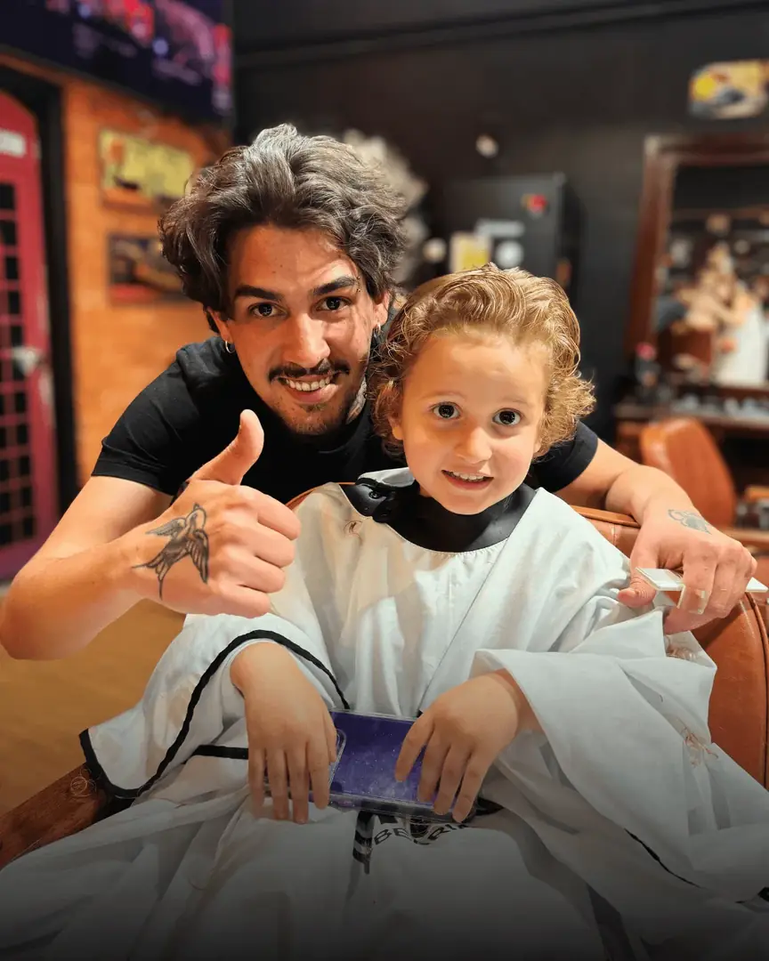 Barbeiro e criança sorrindo na cadeira, com o polegar para cima
