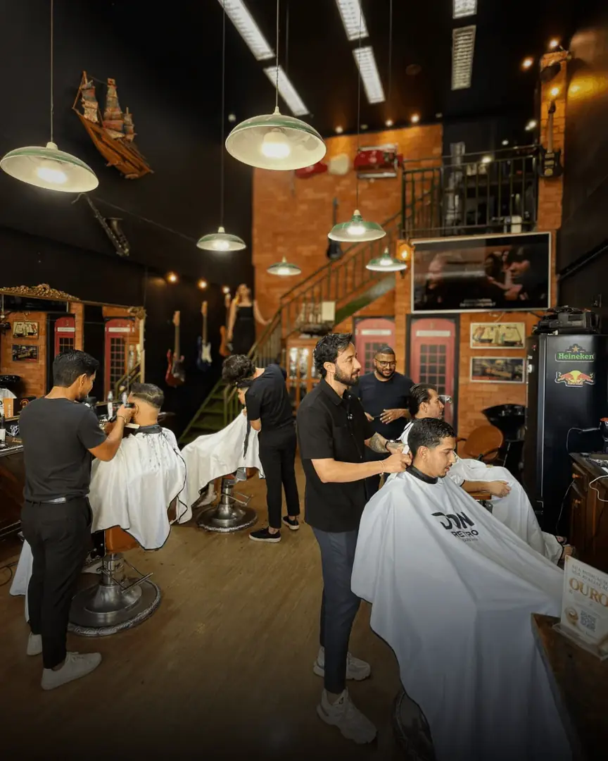 Barbeiros atendendo clientes nas cadeiras, com a escada de tijolos ao fundo