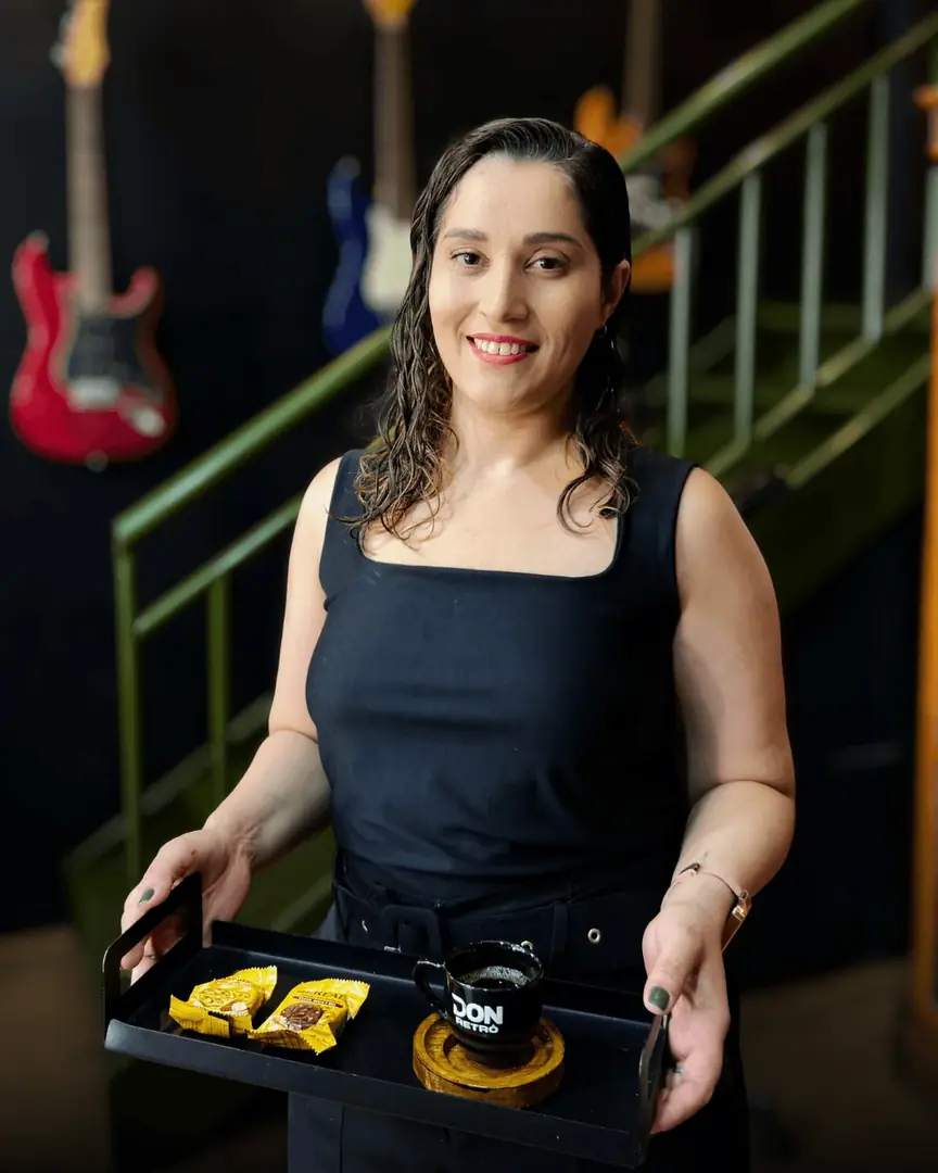 Atendente sorrindo com uma bandeja de petiscos, com guitarras ao fundo