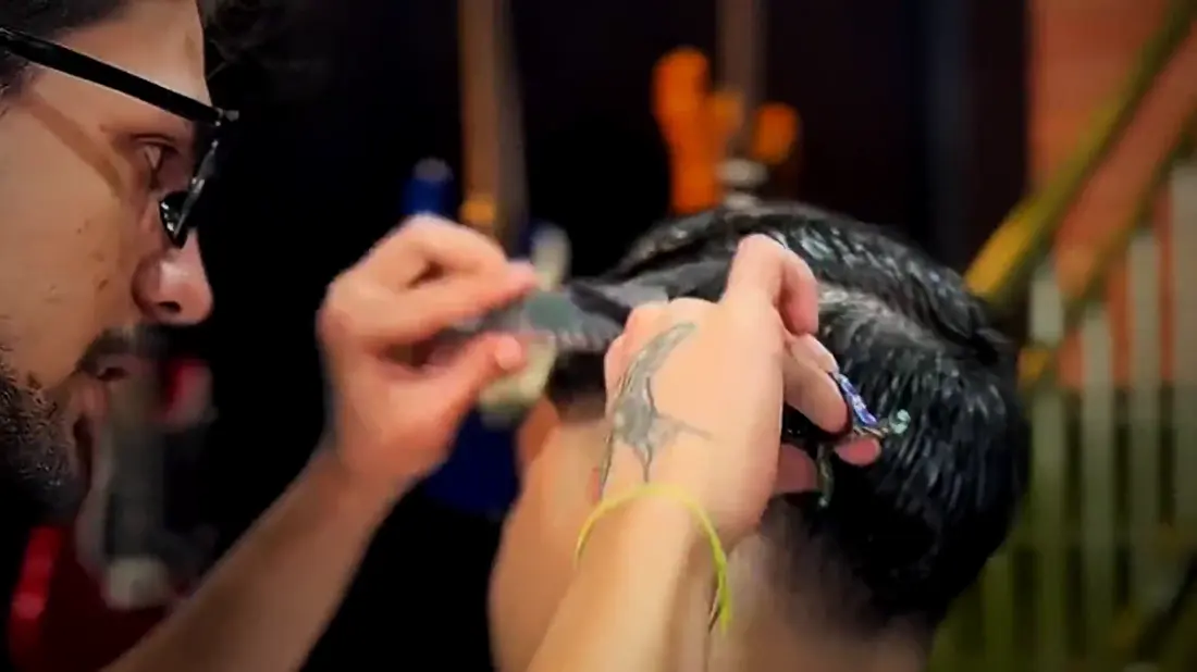 Barbeiro cortando o cabelo de um cliente com tesoura e pente